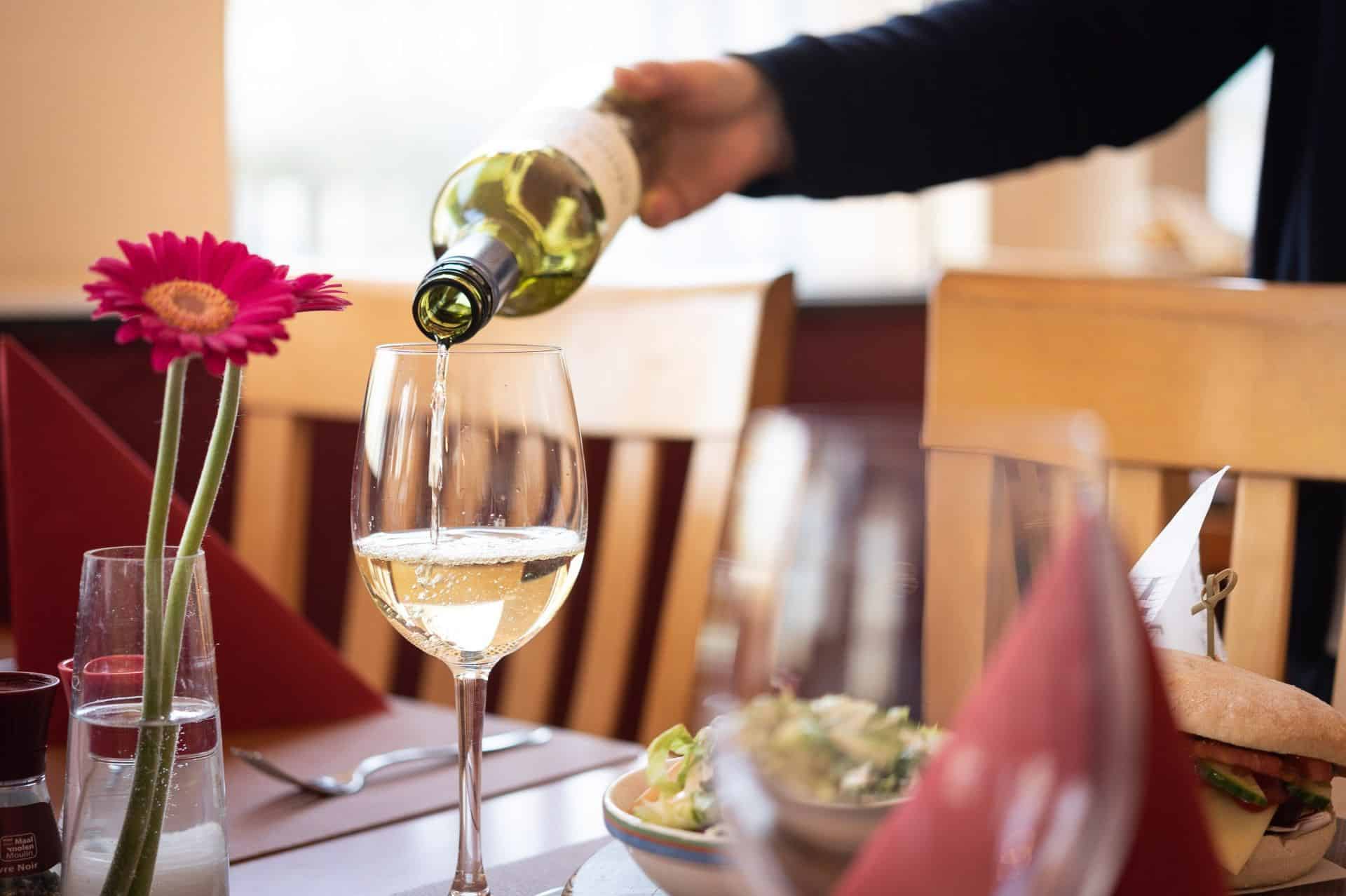 Person, die ein Glas Wein im Restaurant des Green-Park-Hotel-Brügge einschenkt